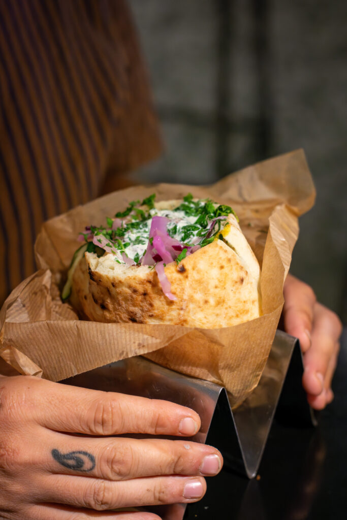 Pita Greek con pargit de pollo, grasa de cordero, col tomate cebolla asada y tzatziki en el restaurante Dos Manos Pita Bar en barri de Gràcia de Barcelona