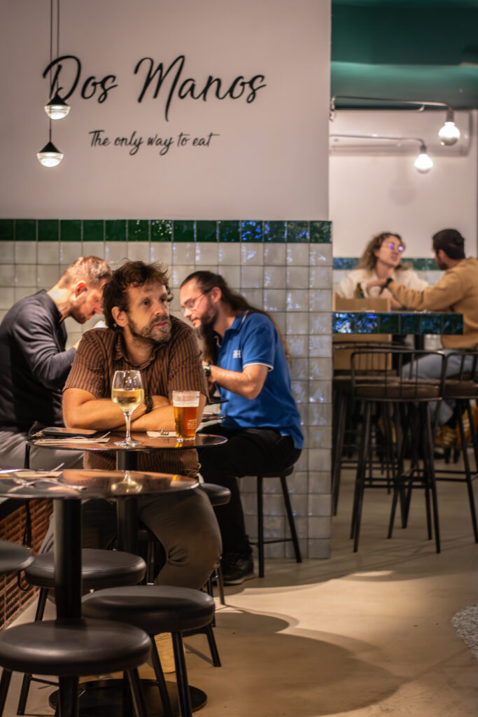 Interior con mesas altas y azulejos verdes del restaurante Dos Manos Pita Bar del barri de Gràcia de Barcelona