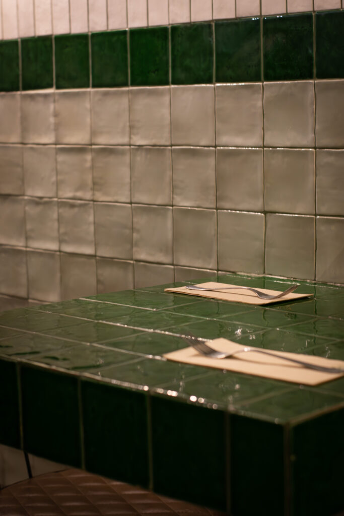 Interior con mesas altas y azulejos verdes del restaurante Dos Manos Pita Bar del barri de Gràcia de Barcelona