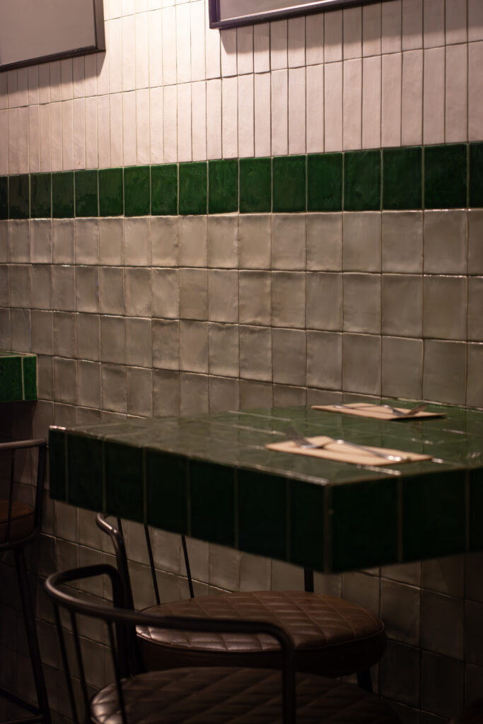 Interior con mesas altas y azulejos verdes del restaurante Dos Manos Pita Bar del barri de Gràcia de Barcelona