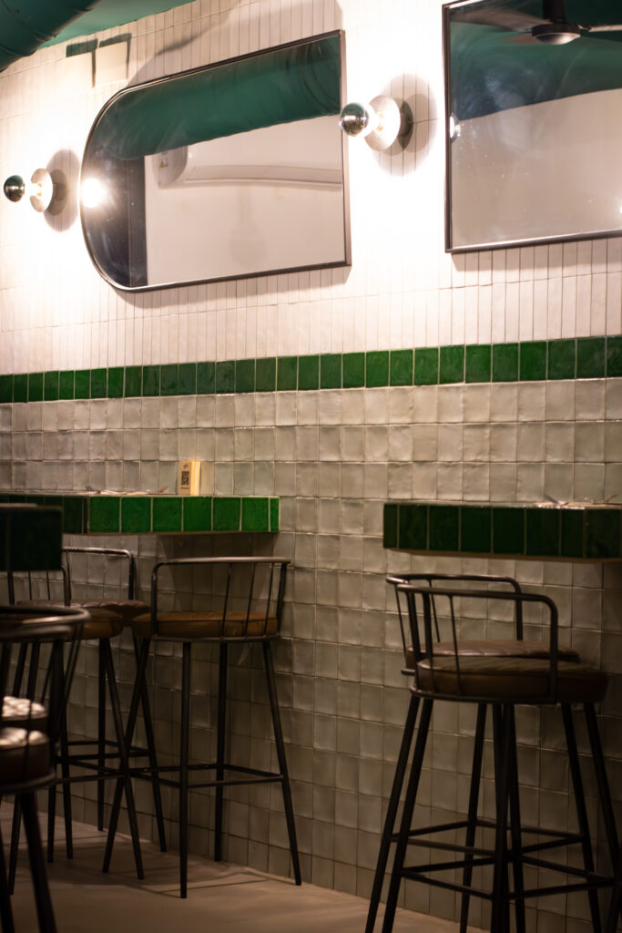 Interior con mesas altas y azulejos verdes del restaurante Dos Manos Pita Bar del barri de Gràcia de Barcelona